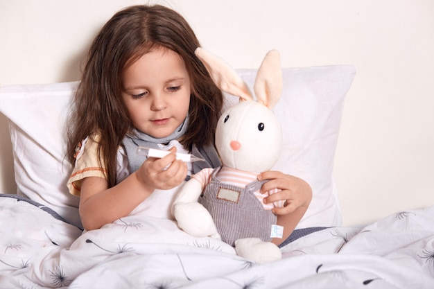 小さな女の子がベッドに横になっていると温度計で柔らかい聞くの温度を測定