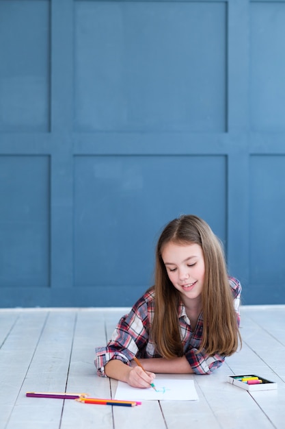 Photo little girl lying on the floor and creating a picture with pencils.