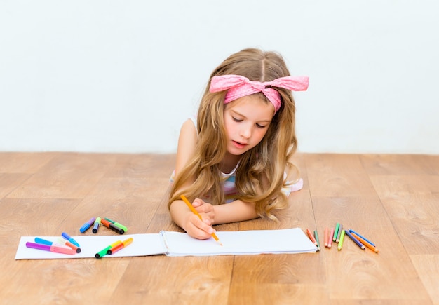 Little girl lying on the floor draws with pencils