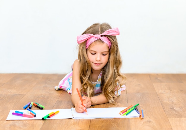 Маленькая девочка, лежа на полу, рисует карандашами