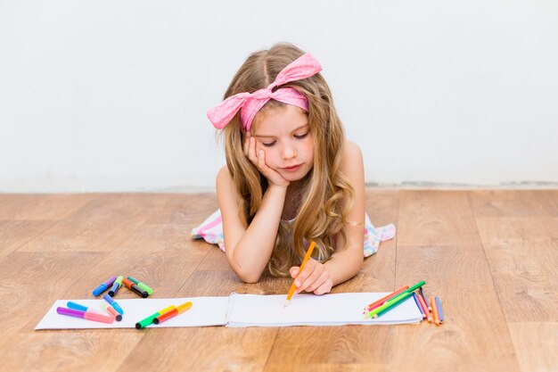 Little girl lying on the floor draws with pencils