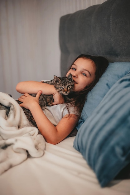 写真 ベッドに横たわって子猫を抱きしめる少女