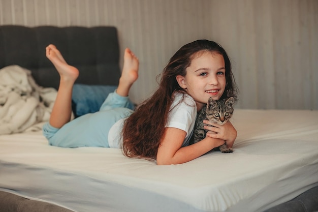 写真 ベッドに横たわって子猫を抱きしめる少女
