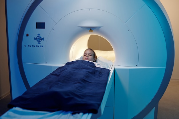 MRI 스캔 기계로 이동하는 동안 긴 의료 테이블에 누워 어린 소녀