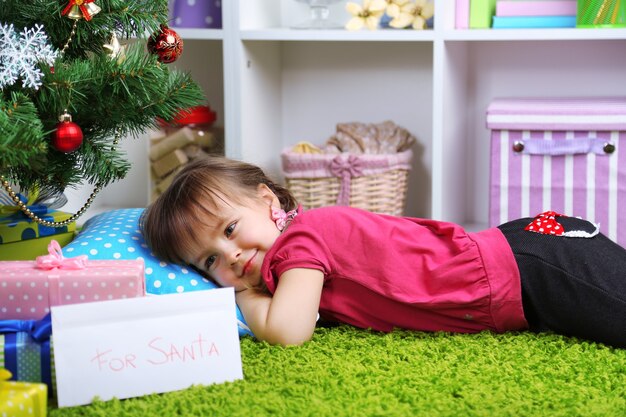 Little girl lying near Christmas tree in room