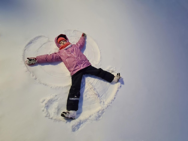 Little girl lying in snow and making angel top view