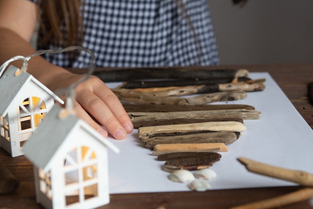 写真 小さな女の子は棒の引っ掛かりと殻の創造性からクリスマスツリーの工芸品を作ります