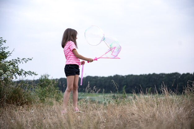 Little girl makes big multicolored soap bubbles on the nature in the field