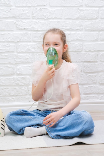 사진 작은 소녀는 침대에 앉아있는 동안 의료 nebulizer로 흡입을합니다 귀여운 아이는 아프습니다