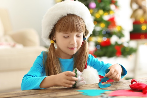 Little girl making felt Christmas fir tree at table