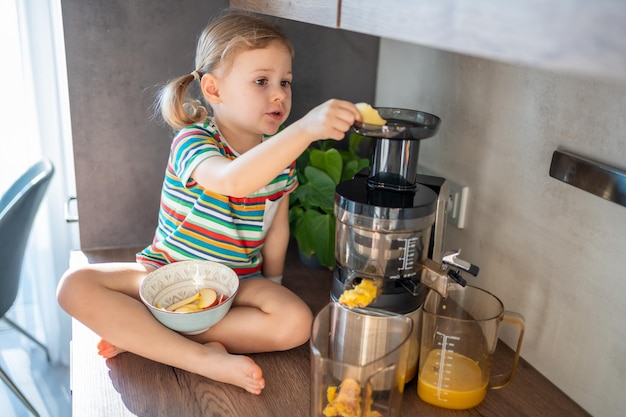 Little girl making fresh juice sitting on the table in home kitchen