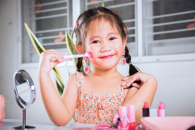 Little girl making makeup her face she look in the mirror and cheek fluffy brush for powder