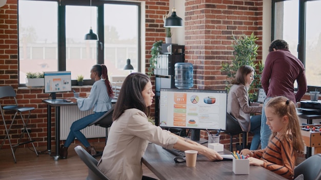 Little girl making noise and disturbing business people at office while working mother trying to plan and project a strategy, do assignment. Stressed woman stopping child from interfering with work