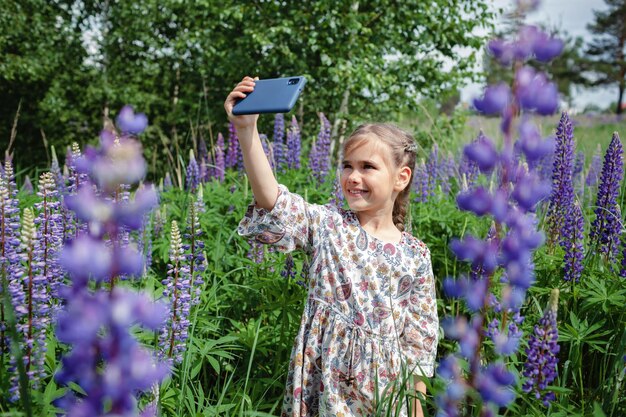 夏に咲くフィールドの若いブロガーで紫色のルピナスの間で自分撮り写真を作る少女