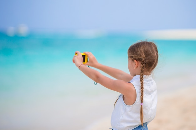 Little girl making video or photo of tropical beach with her camera for the memory