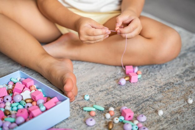 Little girl making wooden beads bracelet at home living room Children's creativity and the development of fine motor skills