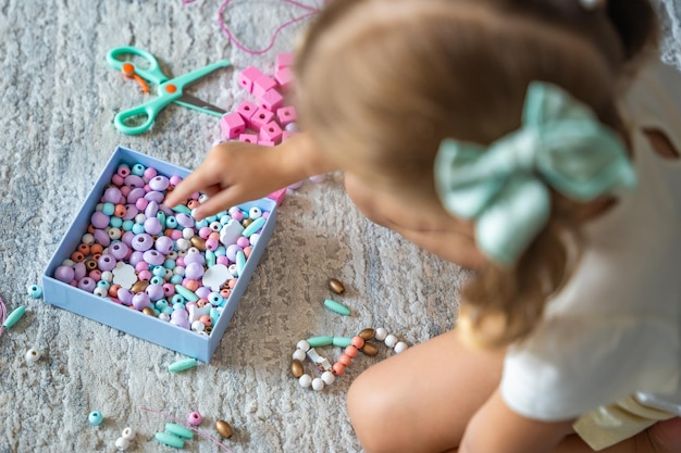 Little girl making wooden beads bracelet at home living room Children's creativity and the development of fine motor skills