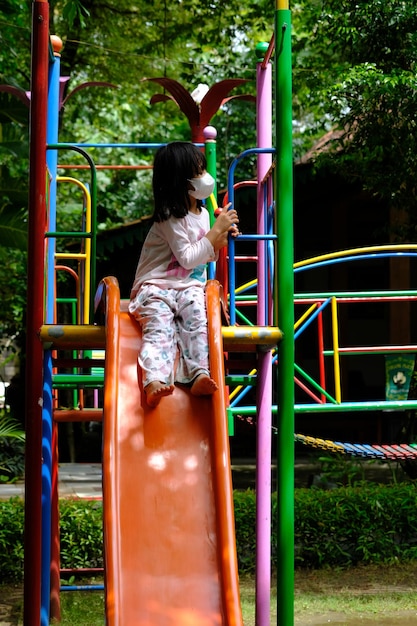 Little girl in a mask playing on the slide. the covid pandemic\
made everyone wear masks. tropical.