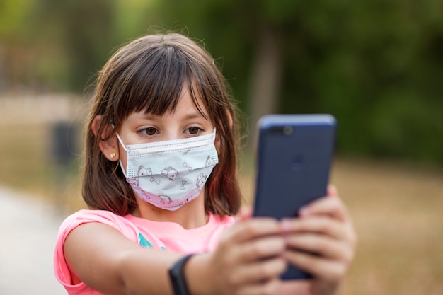 屋外の公園で、彼女の携帯電話を使用してマスクの少女