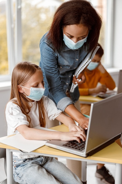 Foto bambina in maschera che utilizza laptop durante la lezione