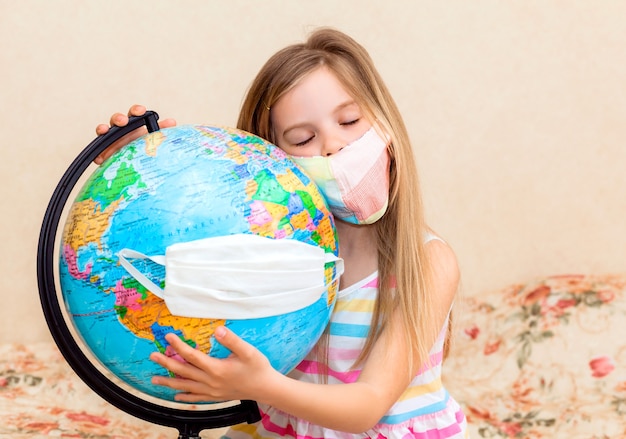 Little girl in a medical mask holds a globe in her hands, wrapped in a medical mask. 
