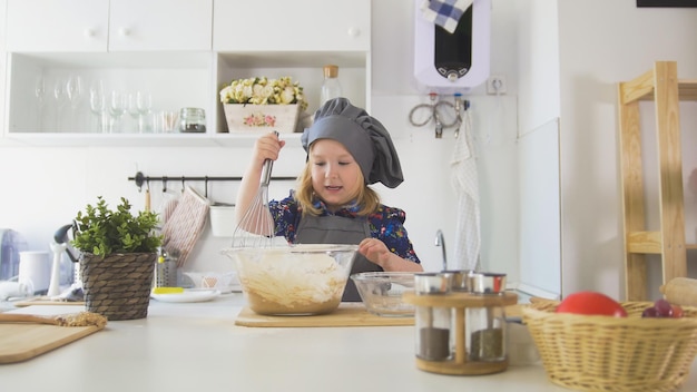 Little girl mixes the mixture for cookies with a big spoon close up