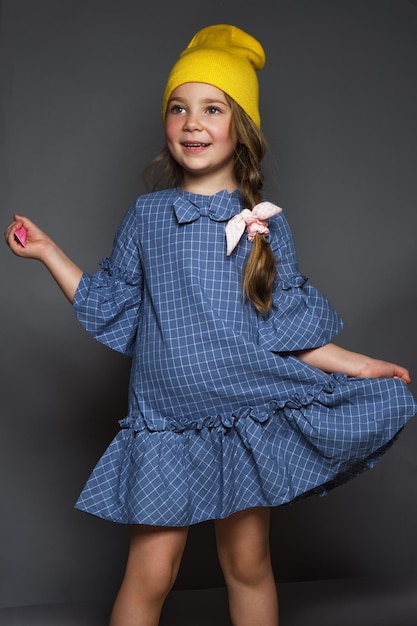 Little girl model professionally posing in the studio in a dress and a yellow hat Model tests