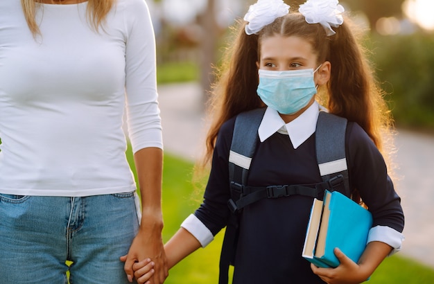 Photo little girl and mom in medical mask during covid-19. mom and daughter go to school.