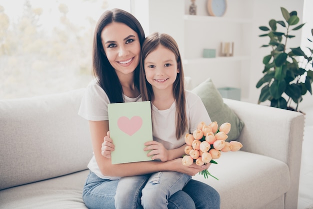 Маленькая девочка мама сидит на уютном диване в доме в помещении держит 8 марта цветы открытки