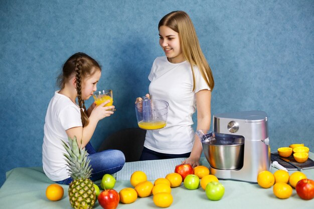 小さな女の子とお母さんは果物からフレッシュジュースを絞り、それを飲みます。