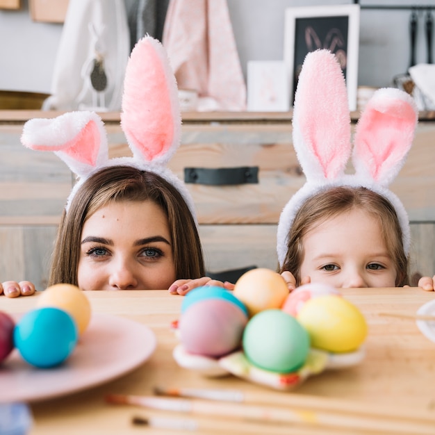 Little girl and mother in bunny ears hiding behind table