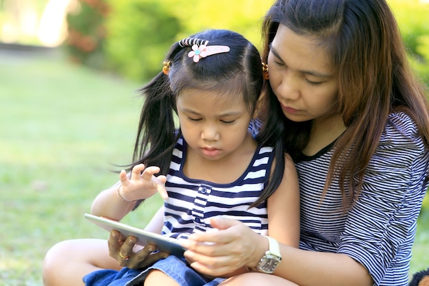 어린 소녀와 어머니는 공원에서 태블릿 PC를 즐길 수 있습니다.