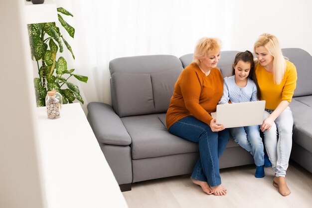 little girl mother and grandmother with laptop while sitting on sofa at home.