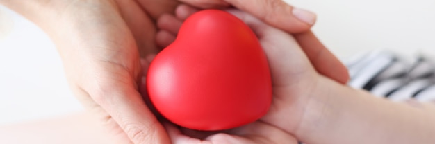 Маленькая девочка и мать руки держат красное игрушечное сердце крупным планом