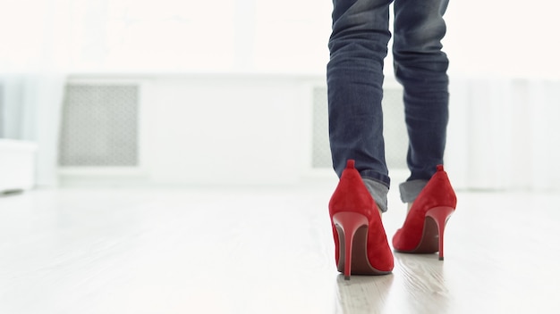 Little girl in mother's red shoes is walking around the house. Back view, copyspace