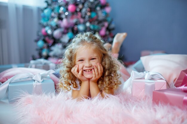 A little girl near the Christmas tree is lying on the bed