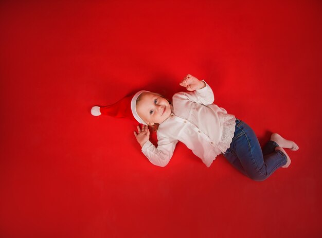 little girl in a New Years hat lies on a red background