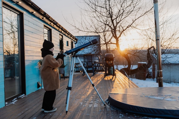 小さな女の子が冬の夕暮れの外で望遠鏡を通して天体を観察している