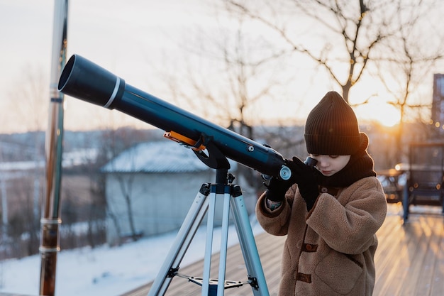 a little girl observes celestial bodies through a telescope outside at sunset in winter