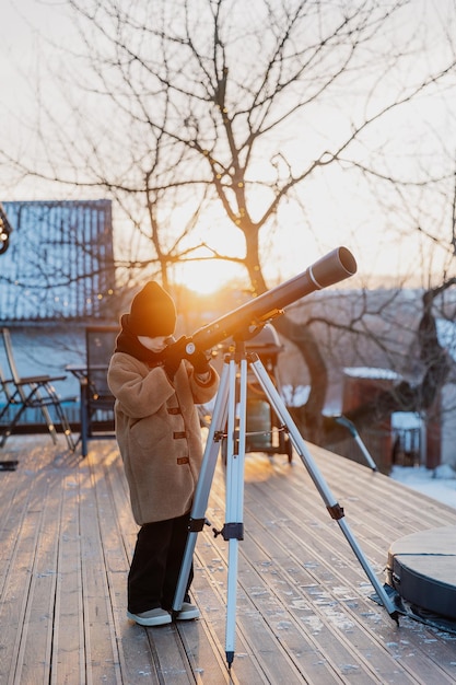a little girl observes celestial bodies through a telescope outside at sunset in winter