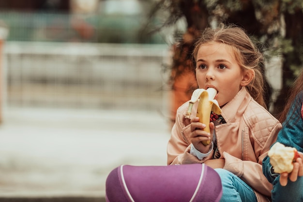 Фото Маленькая девочка на школьном обеденном перерыве ест бананы выборочный фокус фото высокого качества