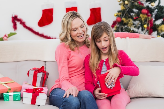 Photo little girl opening a gift at christmas with mother