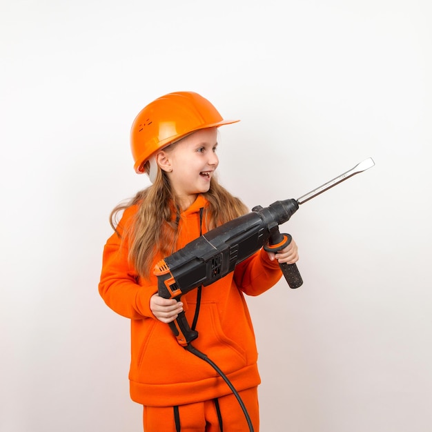 Little girl in an orange suit and construction helmet holding puncher concept of young worker Portrait child builder white background Labor Day