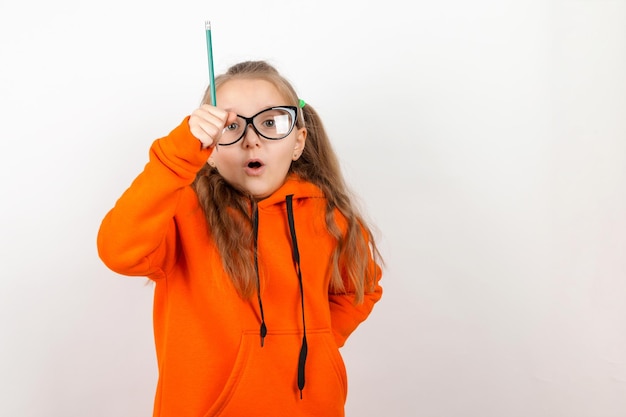 A little girl in an orange suit glasses and pencil The concept of school training selfdevelopment On a white background