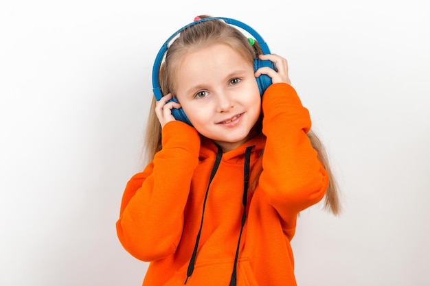 A little girl in an orange suit listening to music in blue headphones on white background