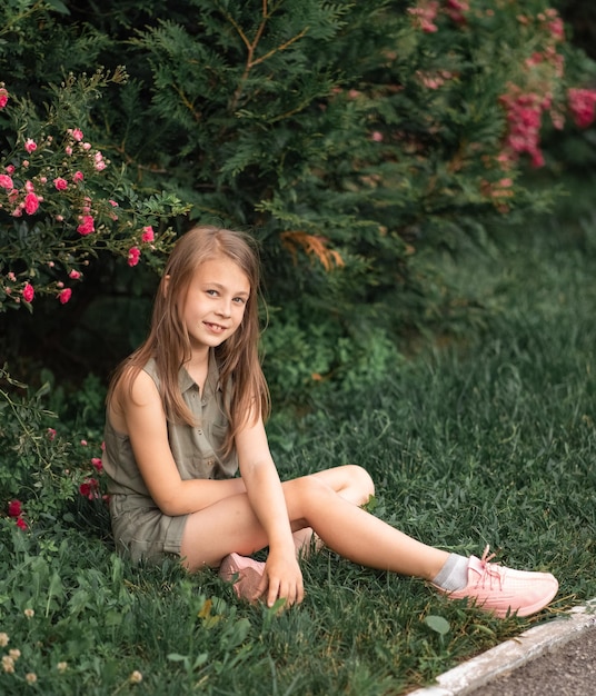 Little girl outdoors sitting near a bush of roses