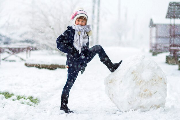 Little girl outdoors in winter near big snow ball