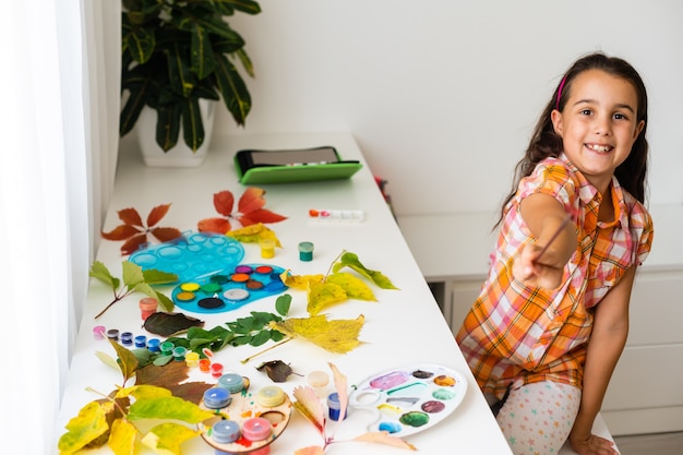 Little girl painting on autumn yellow leaves with gouache, kids arts, children creativity, autumn art.