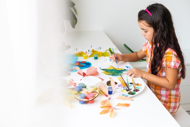 Foto bambina che dipinge su foglie gialle autunnali con gouache, arte per bambini, creatività per bambini, arte autunnale.