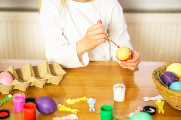 Foto una bambina che dipinge le uova per pasqua sul tavolo di legno a casa preparazione per una buona pasqua